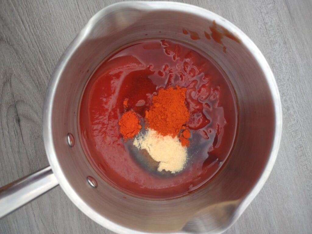 A pot with ketchup and seasonings ready to stir together to make BBQ sauce.