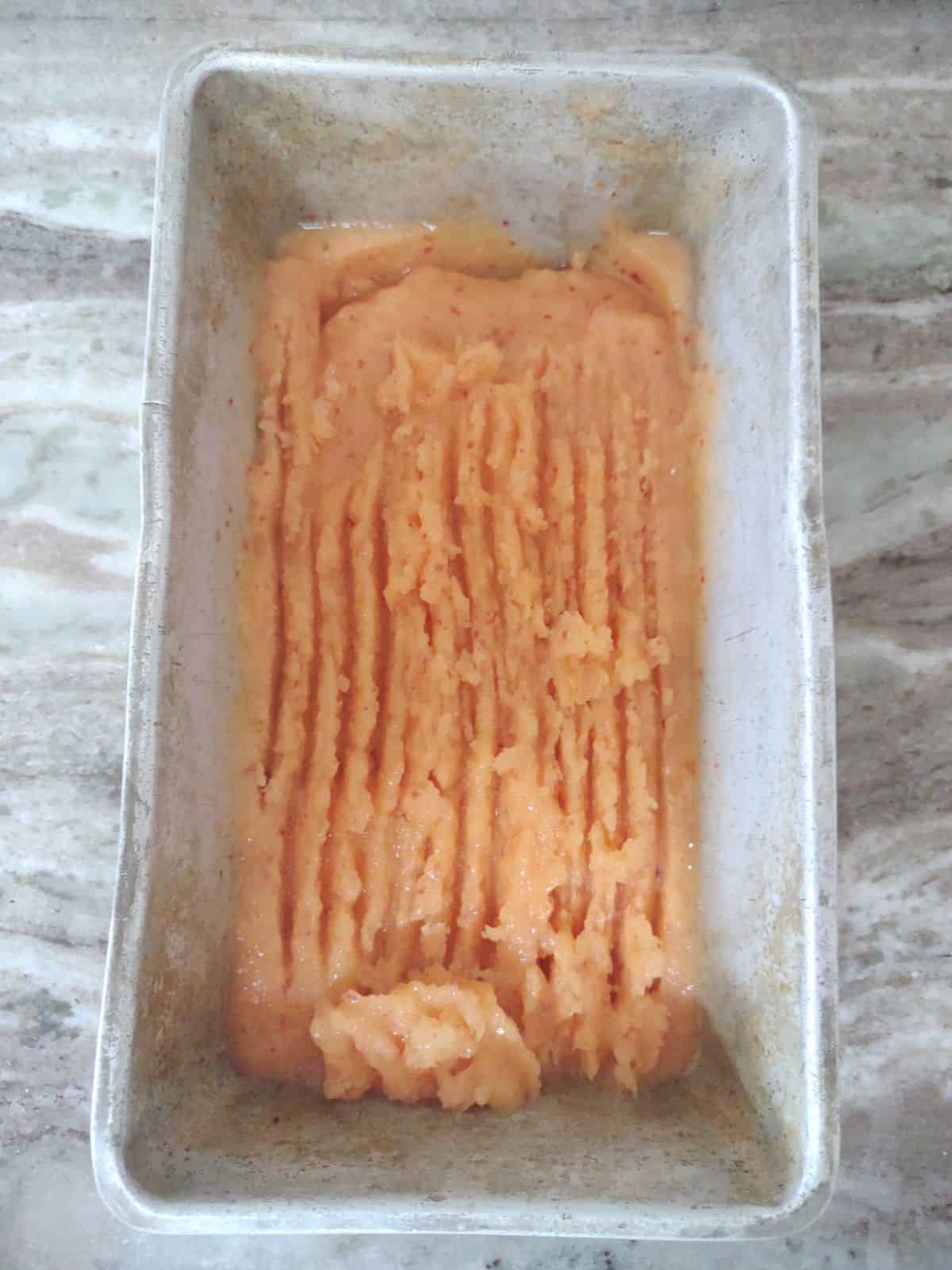 Peach granita that is almost completely frozen in a metal bread loaf pan.