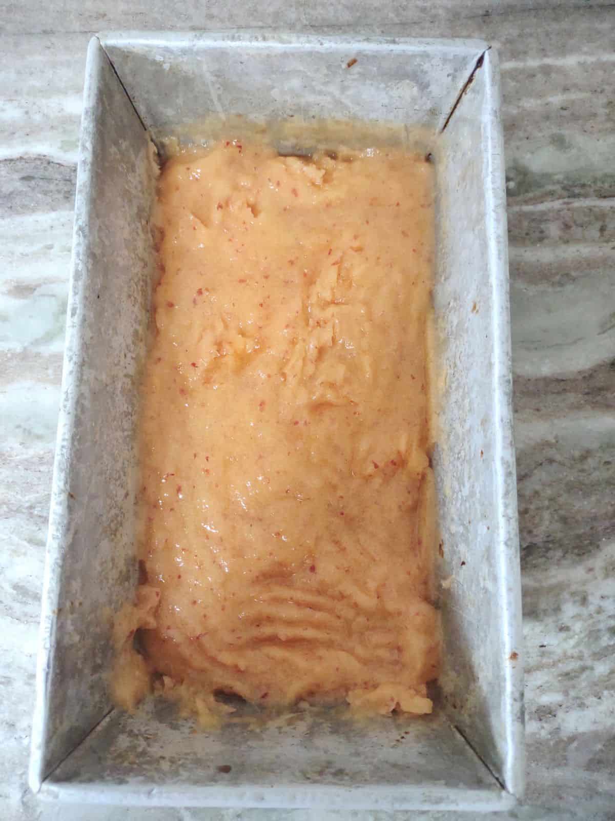 Peach granita that is starting to freeze in a metal bread loaf pan.