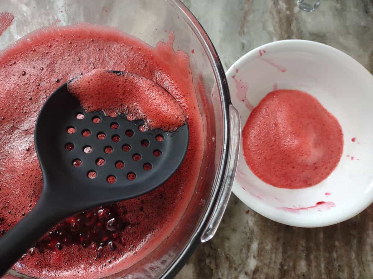 Foam being skimmed off the top of Jell-O with a slotted spoon into a white bowl.