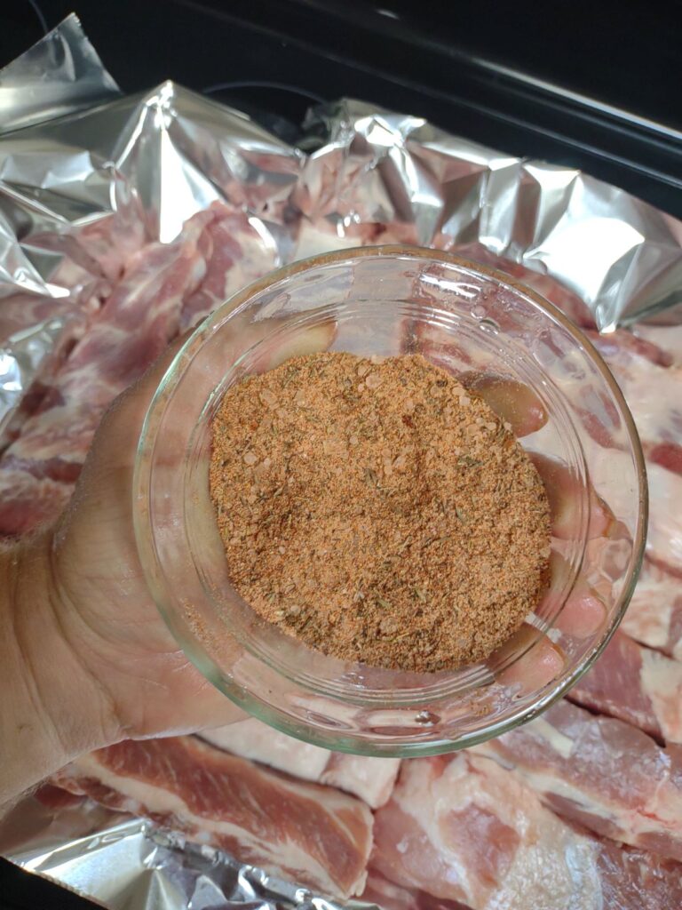 A dry rub in a glass bowl above raw St. Louis pork rib portions.