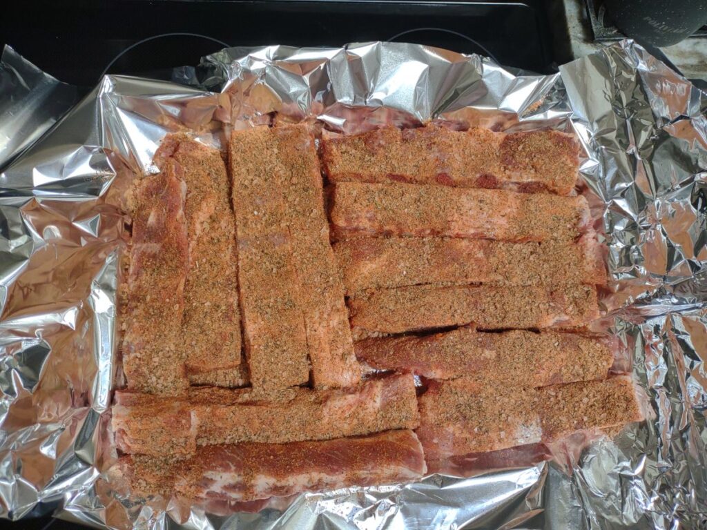 Raw St. Louis Pork Rib portions with a dry rub on it sitting on some foil.
