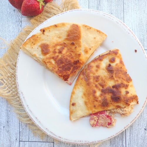 A strawberry cheesecake quesadilla with strawberries, cream cheese filling, and crushed graham crackers on a plate.