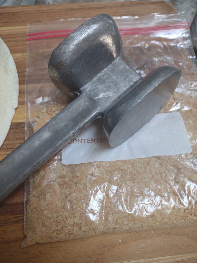 A mallet that is crushing graham crackers in a bag.