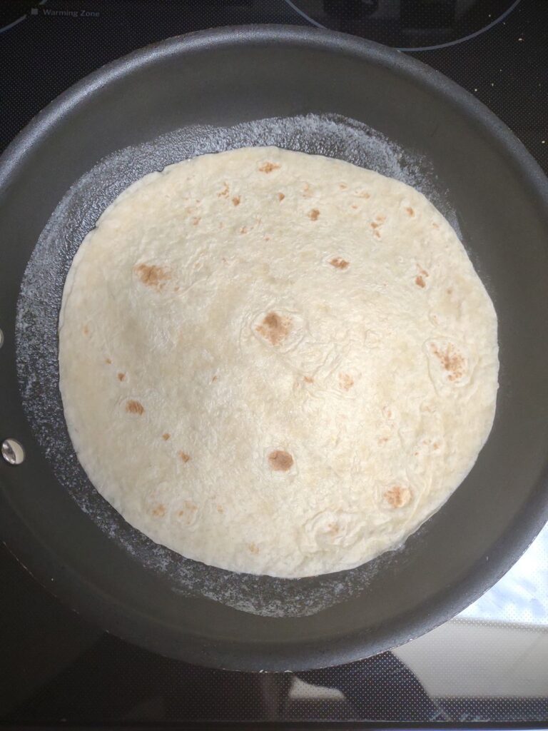 A blueberry cheesecake quesadilla being cooked in a frying pan.