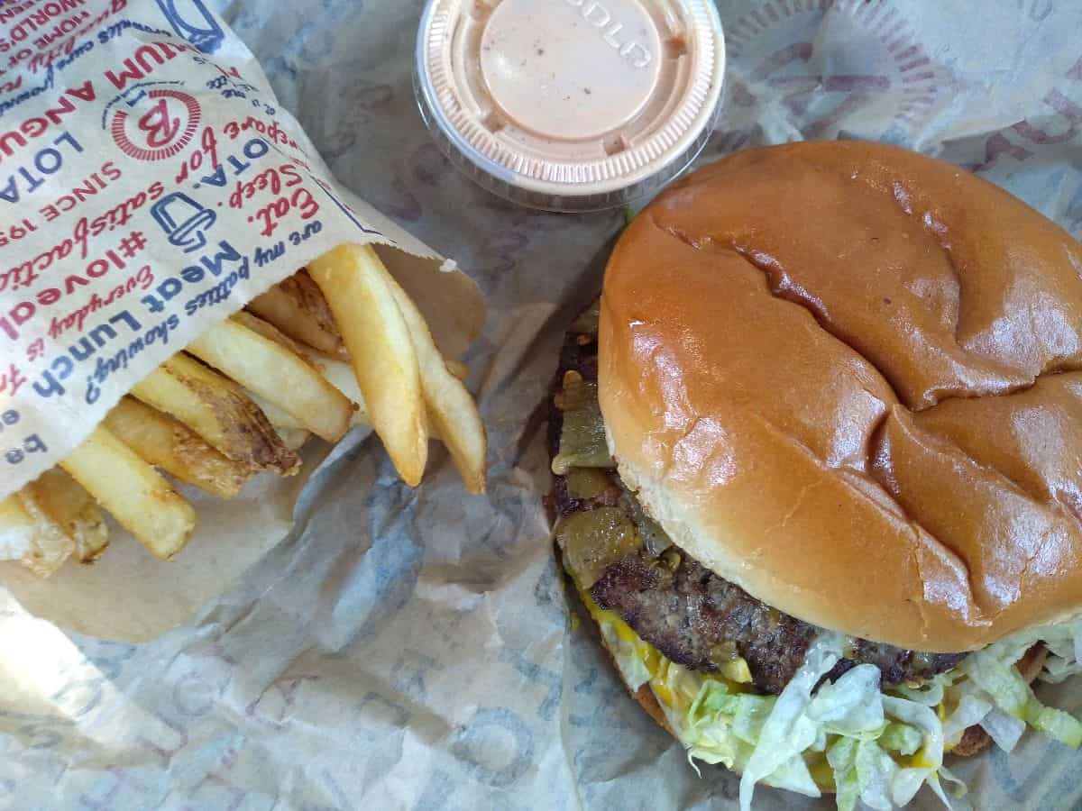 A burger from Blake's Lotaburger with Hatch chiles on it served with a sauce and fries.