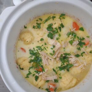 Chicken and dumplings with carrots, celery, and parsley in a white slow cooker.