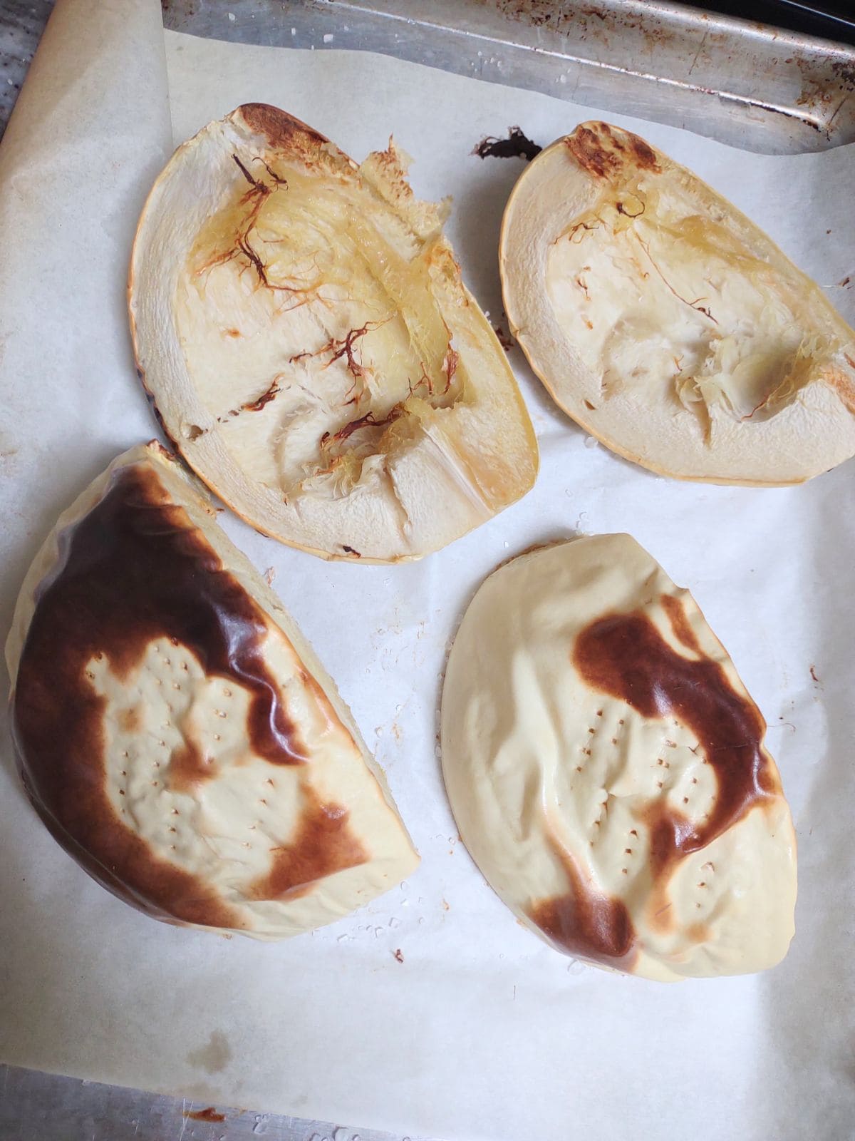 Quartered white pumpkins on a sheet pan after roasting.