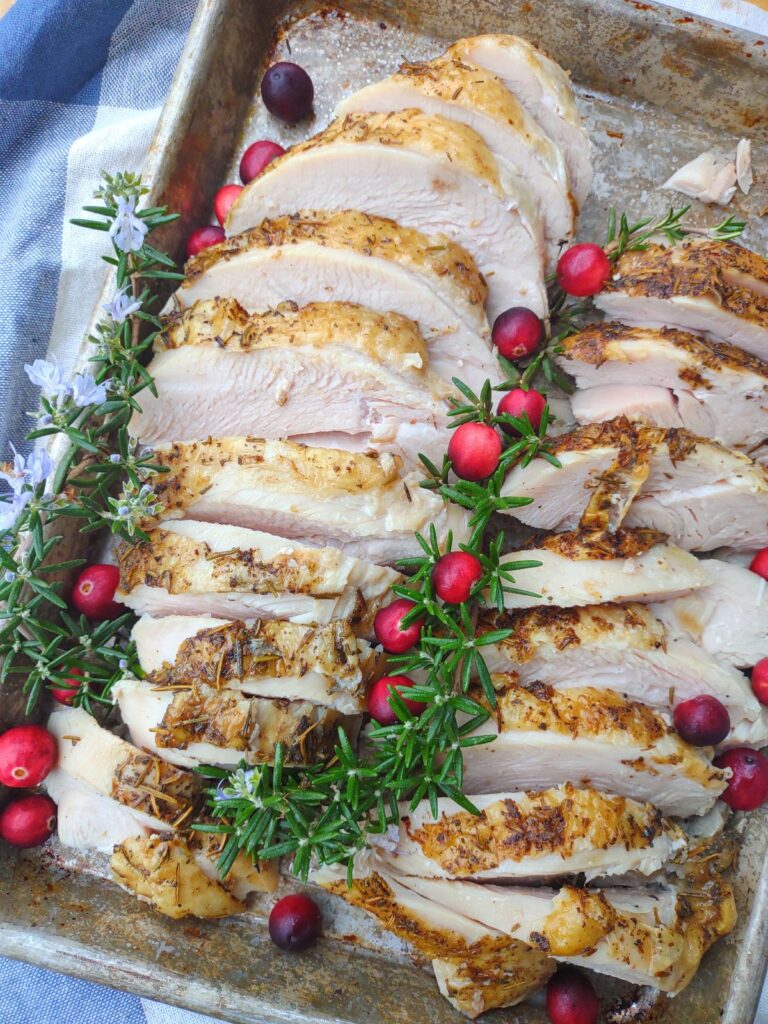 Juicy turkey breast cooked in the Instant Pot arranged on a sheet pan with fresh rosemary and cranberries.