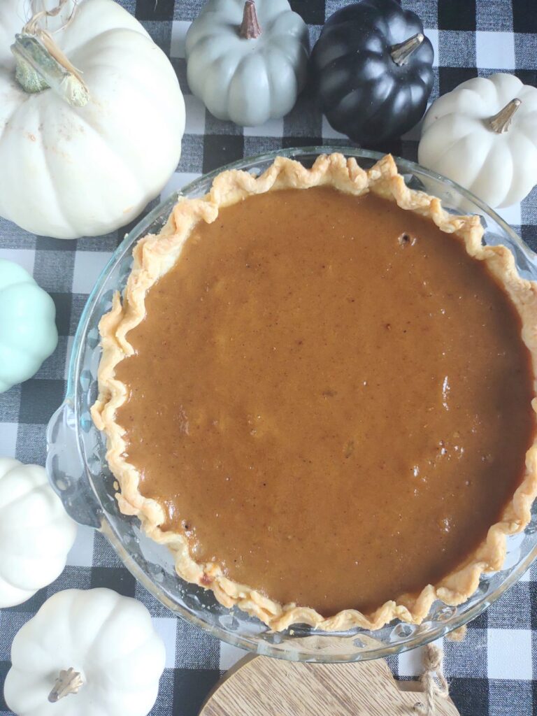 Overhead view of a Creamy homemade pumpkin pie with flaky crust in a pie pan, autumn decor with mini white pumpkins in background.