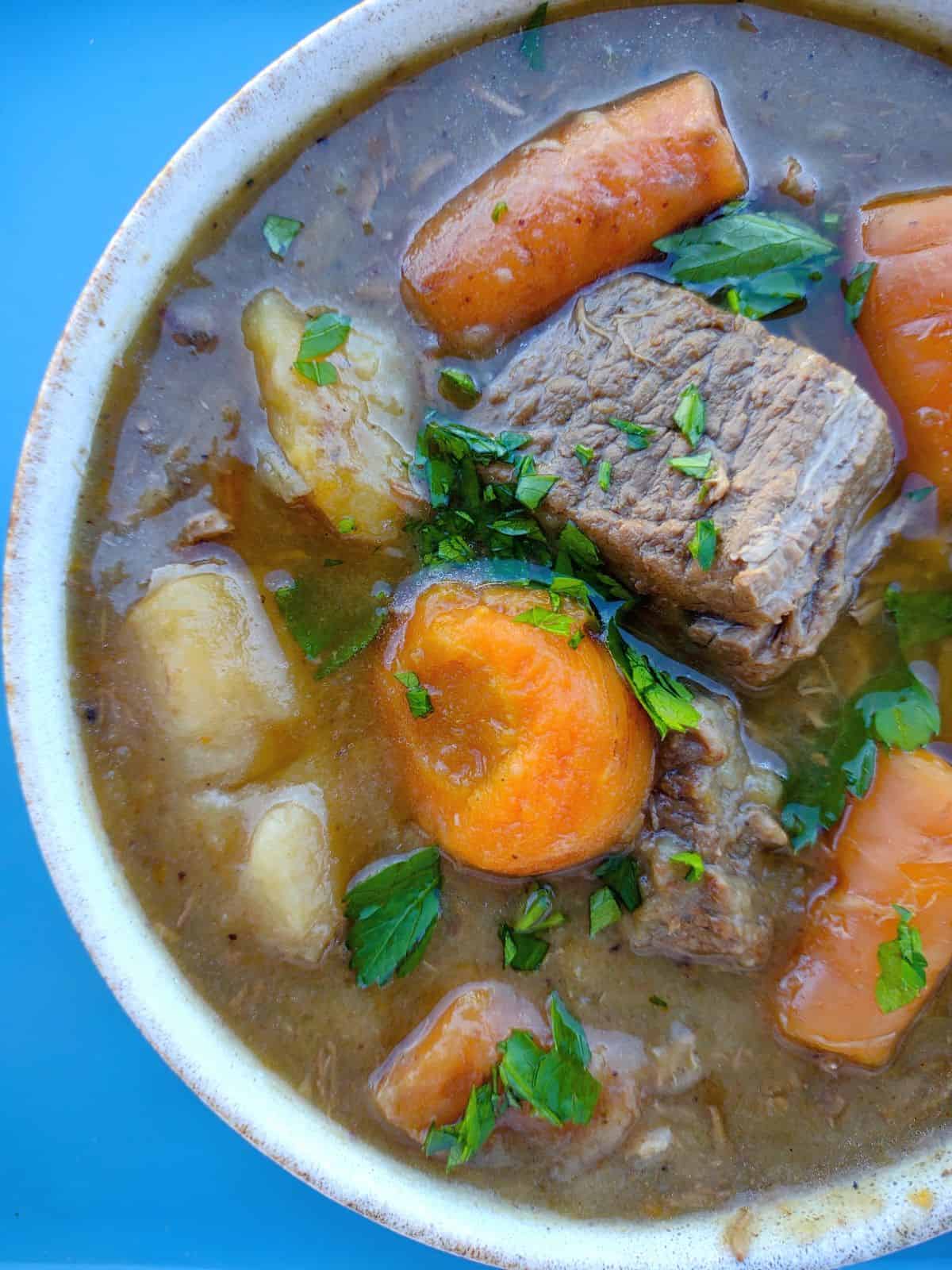 Close up of a bowl of beef stew that was thicken by potato flakes and contains beef stew meat, carrots, potatoes, and parsley.