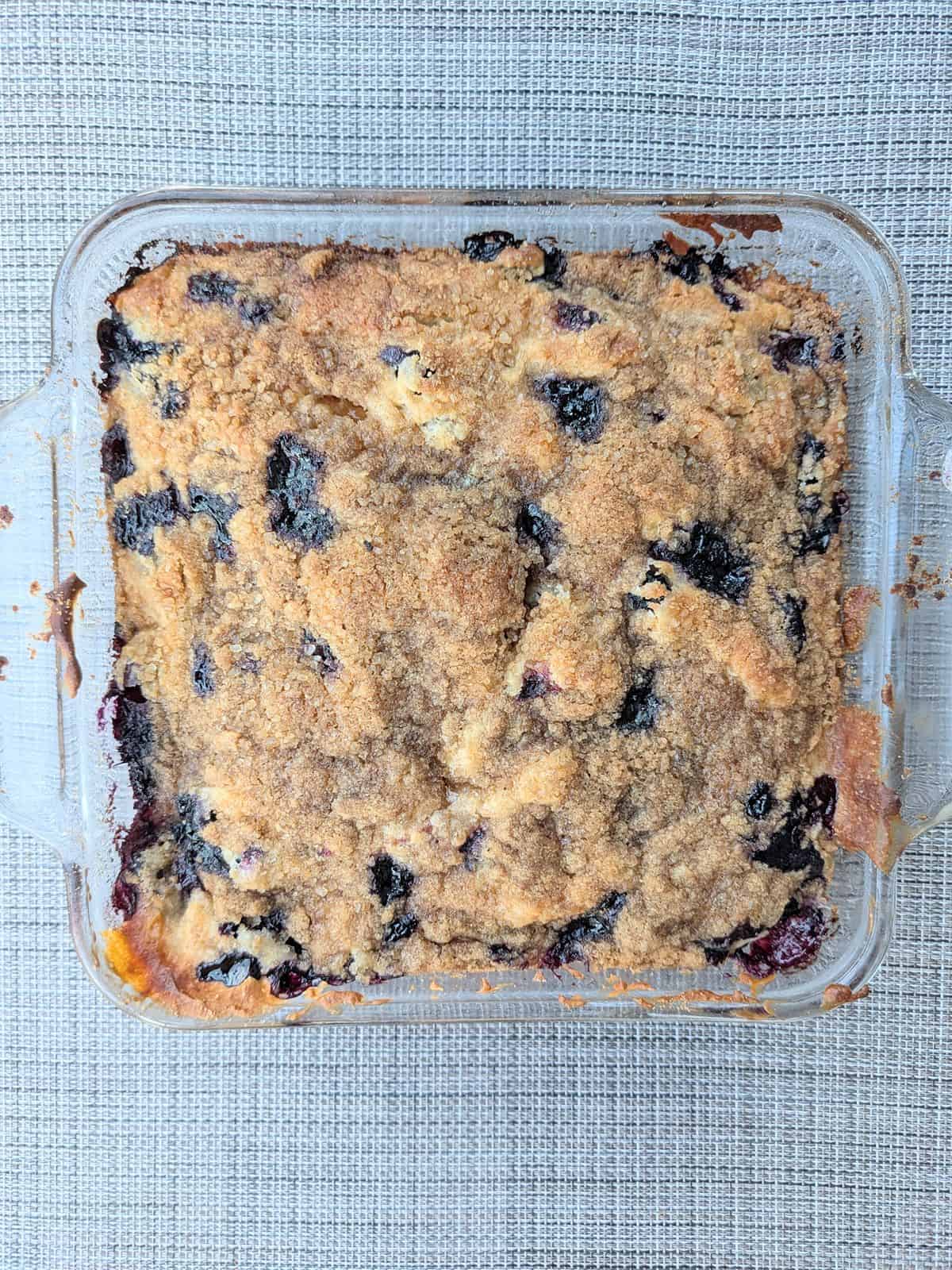 An overhead view of a blueberry-peach buckle in a square glass pan fresh out of the oven.