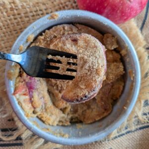A single serving air fryer apple cobbler in a small round cake pan with a black fork.
