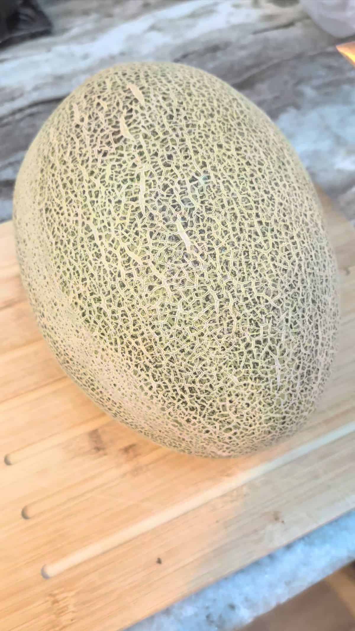 A Waterloupe melon sitting on a cutting board ready to be cut.