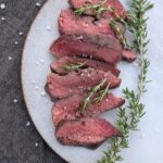 Sliced sous vide flat iron steaks cooked medium rare topped with fresh rosemary and flake salt.