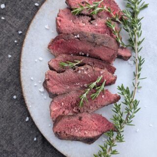 Sliced sous vide flat iron steaks cooked medium rare topped with fresh rosemary and flake salt.